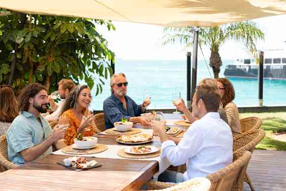 En gruppe mennesker nyter mat og drikke på en terrasse med havutsikt