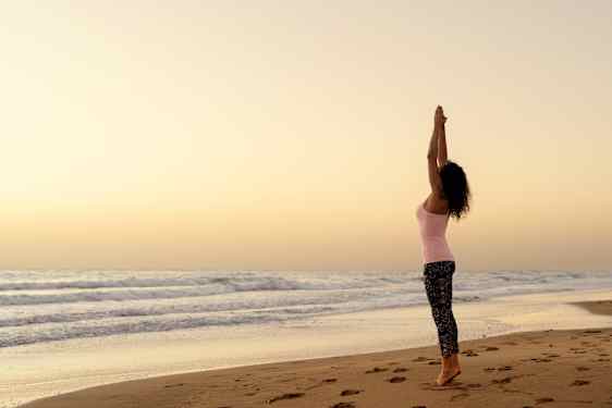 Kvinne trener yoga på stranden ved havet på Gran Canaria.