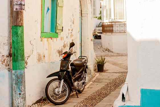 En moped står parkert mellom hvitkalkede småhus i en trang gate.