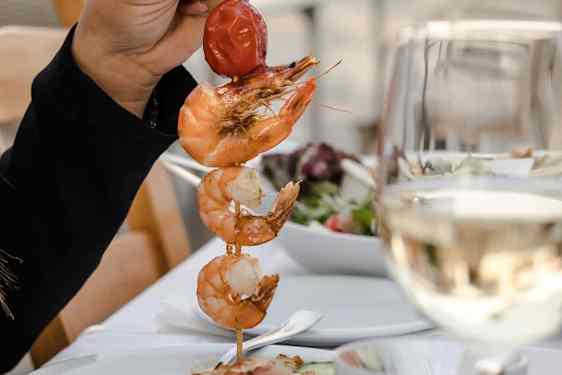 Spyd med grillede reker og tomat servert ved et restaurantbord.