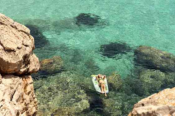 Dame soler seg på madrass i havet, med en restplass i april
