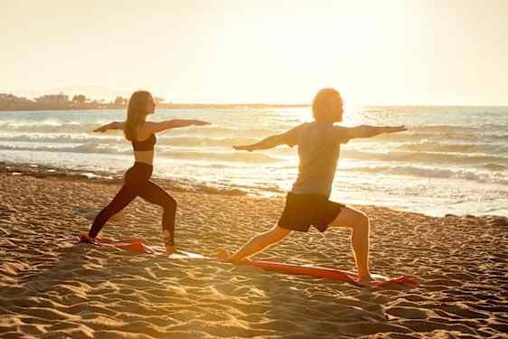 Mann og kvinne gjør yoga på stranden i soloppgangen