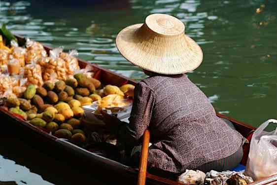 Kvinne i sin båt på vannet som selger ferske thailandske frukter.