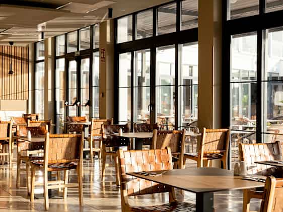 Lys restaurant med store vinduer, bord og stoler i moderne design.