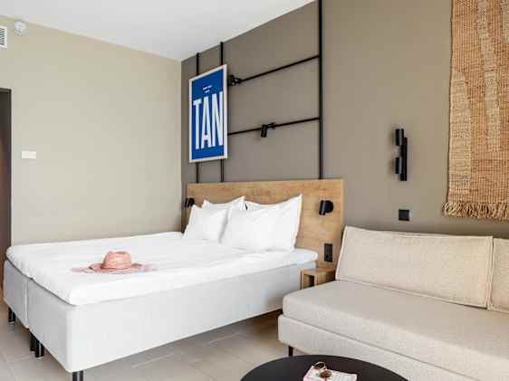 Moderne og lyst hotellrom med dobbeltseng, sofa og stilren innredning.