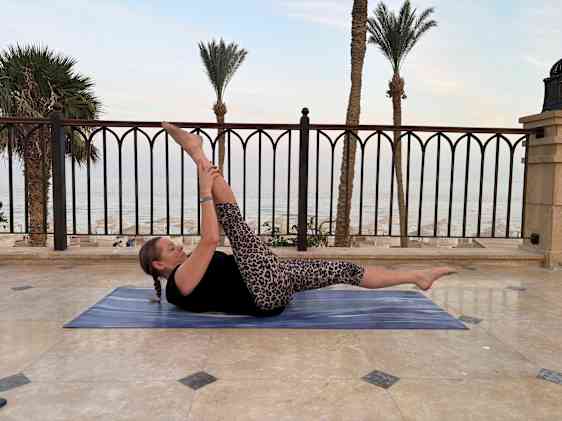 Person som gjør yoga på en matte utendørs med utsikt mot havet og palmetrær.