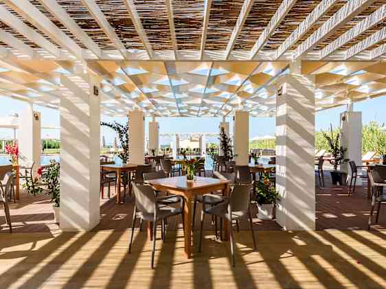 Lys og luftig restaurantterrasse med trepergola, planter og utsikt mot havet.