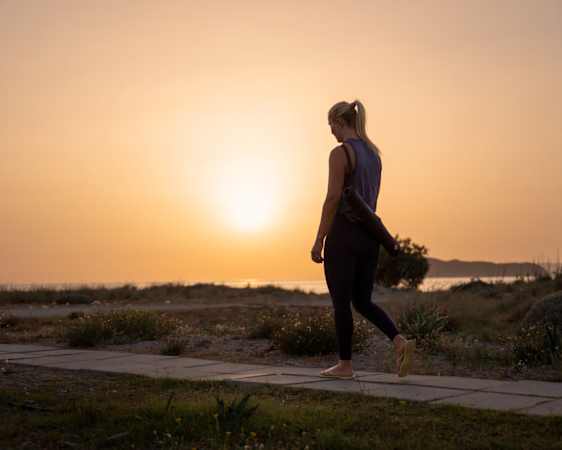 Person med yogamatte på ryggen går langs kysten i solnedgang