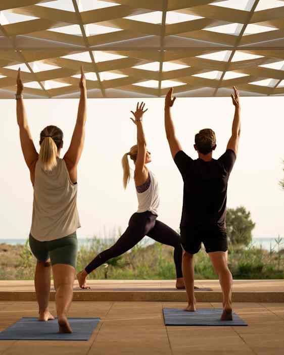 Fem personer gjør yoga på matter i et lyst, åpent lokale med utsikt mot havet.