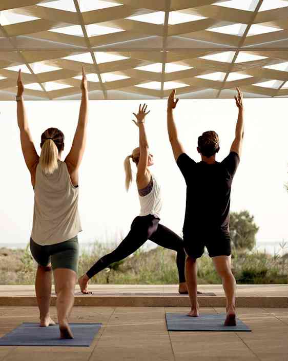 Personer gjør yoga med armene løftet utendørs med tak over seg.