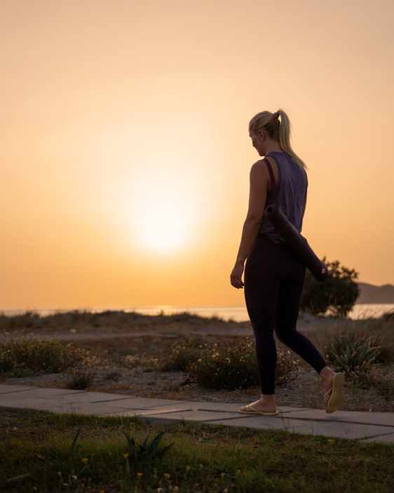 Person går på en sti i solnedgangen med yogamatte under armen.