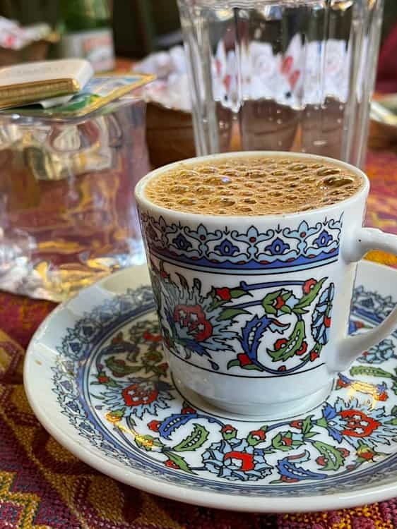 En kopp med fargerikt blomstermønster står på en matchende skål, fylt med kaffe med små bobler på toppen.