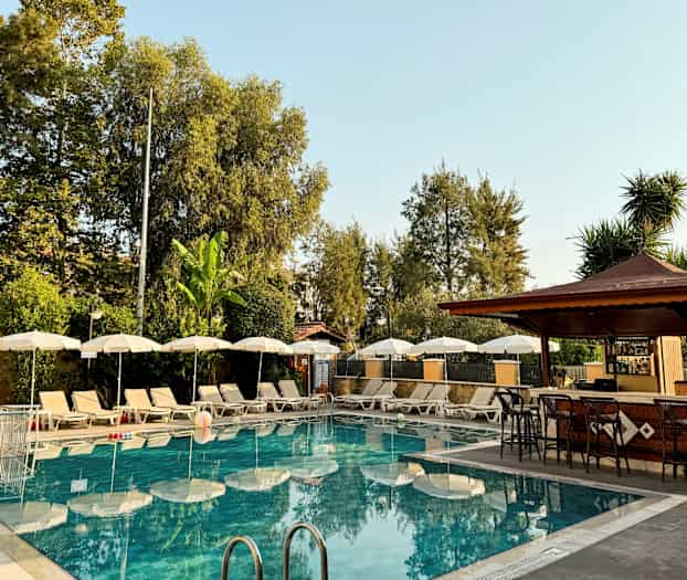 Utendørsbasseng med solsenger og parasoller ved siden av en bar. (AI-generert tekst)