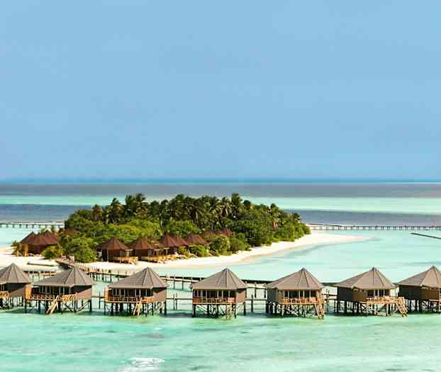 Flere bungalower på påler over vannet ved siden av en frodig øy. (AI-generert tekst)