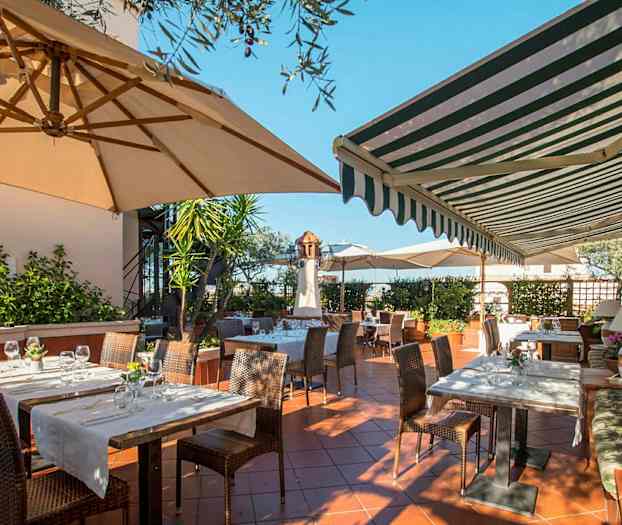 En uteservering med bord og stoler under parasoller og markiser. (AI-generert tekst)