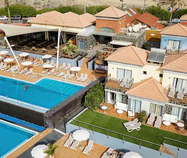 Flere bygninger med oransje tak rundt et utendørs basseng og solsenger. (AI-generert tekst)