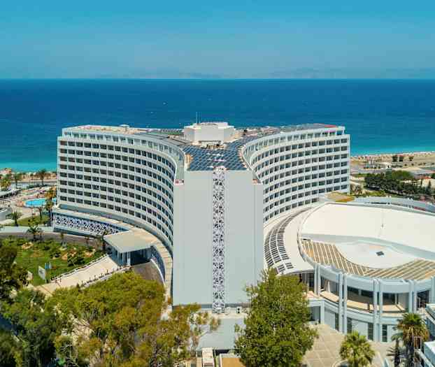 Hotellet med havet og stranden i bakgrunnen. (AI-generert tekst)
