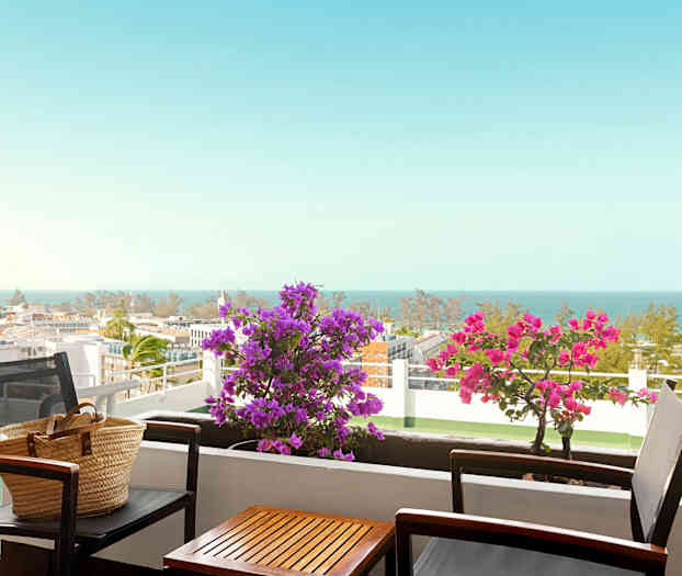 En balkong med bord og stoler, blomster og havutsikt. (AI-generert tekst)