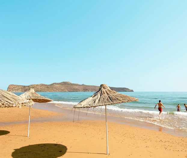 Strand med parasoller av siv og mennesker som bader i havet. (AI-generert tekst)