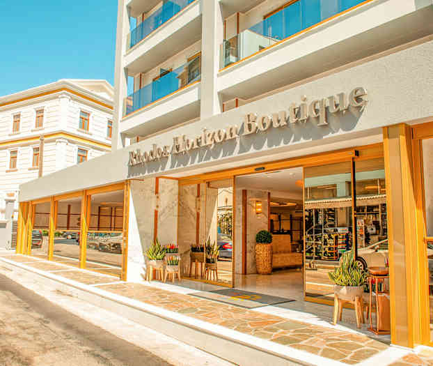 Forsiden av et hotell med navnet Rhodos Horizon Boutique, med glassdører og planter ved inngangen. (AI-generert tekst)