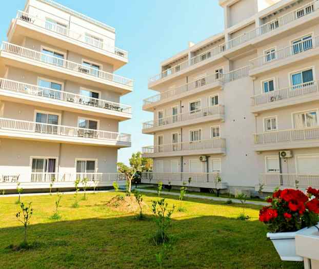 Bilde av to moderne flerfamiliehus med plen og små plantede trær i forgrunnen. (AI-generert tekst)