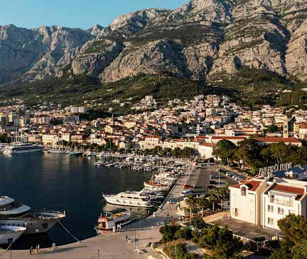 Utsikt over en havn med båter og en by med fjell i bakgrunnen. (AI-generert tekst)