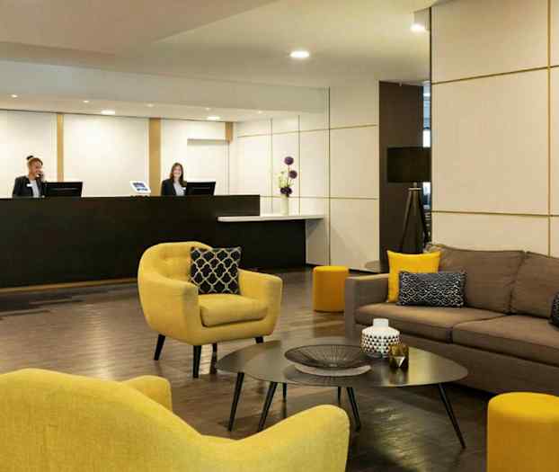 Et hotellobby med sofaer og lenestoler samt et resepsjonsområde. (AI-generert tekst)