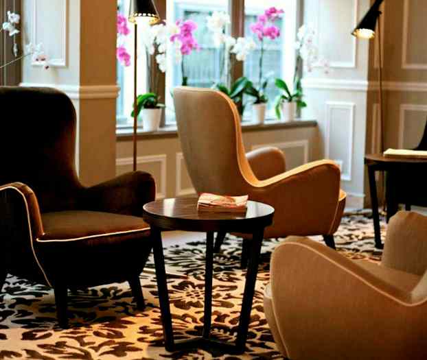 En lounge med komfortable lenestoler, et bord og dekorative blomster i vinduene. (AI-generert tekst)