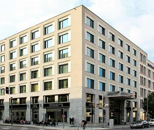 Et hjørnebygg med moderne fasader og store vinduer, med restaurant og bar i første etasje. (AI-generert tekst)