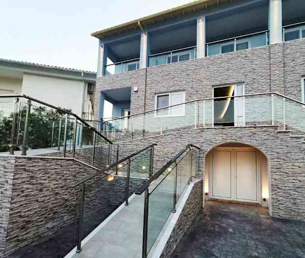 En bygning med steinfasade, glassrekkverk og en trapp. (AI-generert tekst)