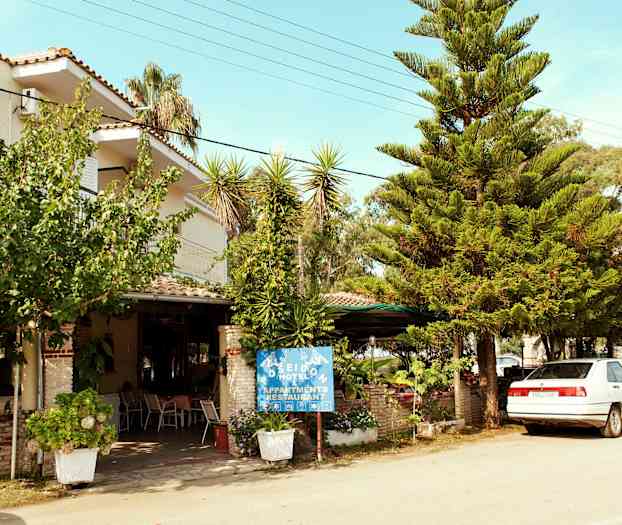 Fotografi av hotellfasade med trær og en parkert bil foran. (AI-generert tekst)