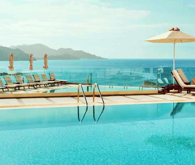 Et infinitybasseng med utsikt over havet og fjellene, omgitt av solsenger og parasoller. (AI-generert tekst)