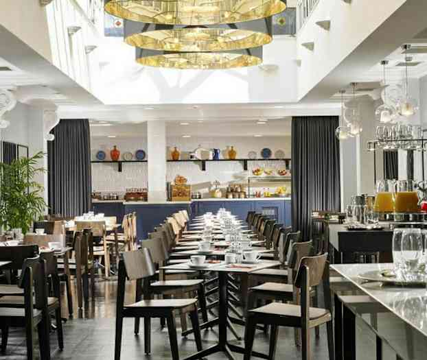 En moderne innredet kafé eller restaurant med bord og stoler, en serveringsdisk og dekorasjoner som planter og hengende lamper. (AI-generert tekst)