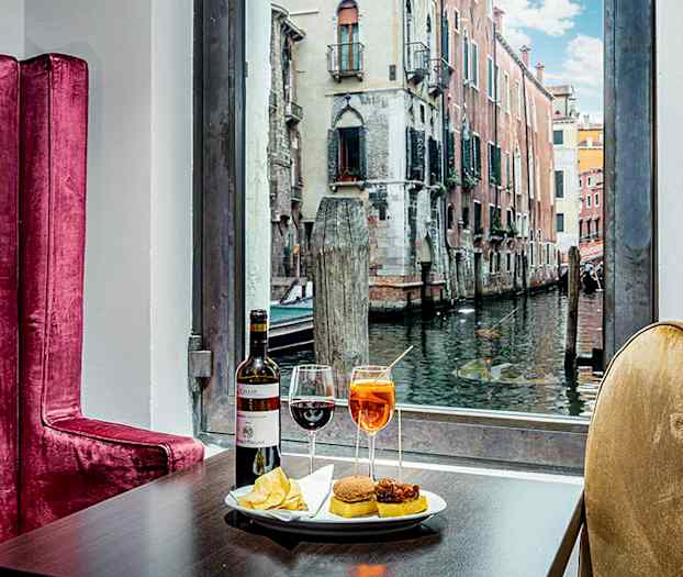 Bord med drikkevarer og snacks, bak ses en kanal med bygninger. (AI-generert tekst)