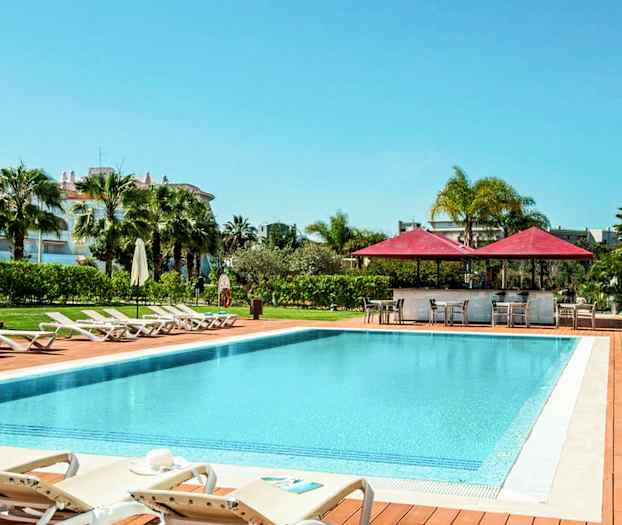 Utendørs basseng med solsenger og parasoller, omgitt av grøntområder. (AI-generert tekst)