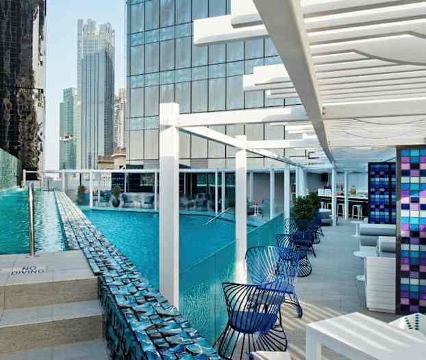 Et moderne utebasseng omgitt av høye bygninger med sittegrupper ved siden av. (AI-generert tekst)