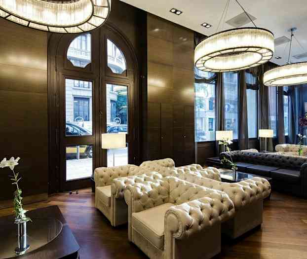 En elegant stue med sittegruppe i Chesterfield-stil, store vinduer, lysekroner og tregulv. (AI-generert tekst)