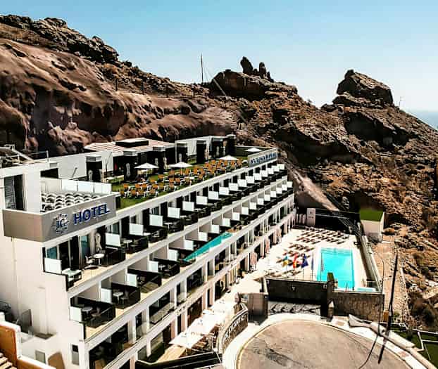 Et hotell plassert ved en fjellskråning med et bassengområde og havutsikt. (AI-generert tekst)
