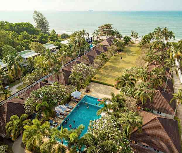 Luftfoto av en ferieanlegg med bungalower, basseng, palmer og havutsikt. (AI-generert tekst)