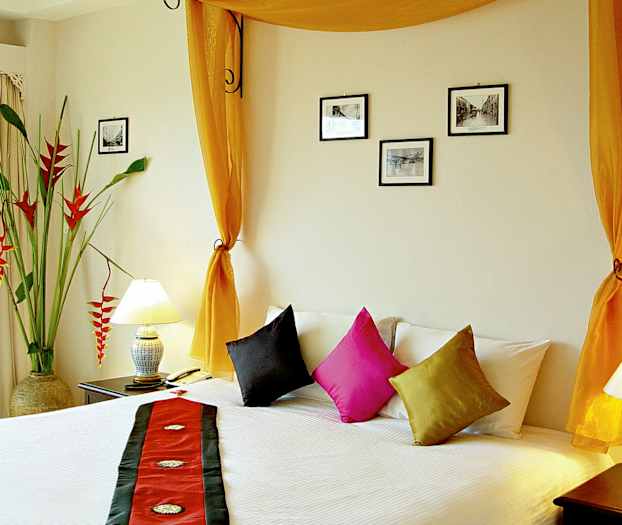 Rom med en seng, dekorative puter, oransje gardiner og veggdekorasjoner. (AI-generert tekst)