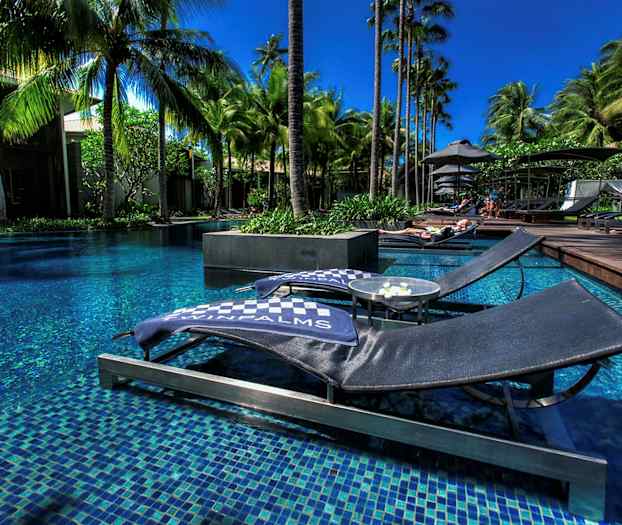 Bilde av solsenger ved et basseng omgitt av palmer. (AI-generert tekst)