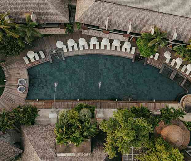 Luftfoto av et basseng omgitt av solsenger, parasoller og frodig vegetasjon. (AI-generert tekst)