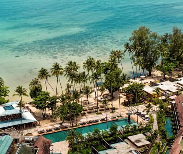 Flyfoto av et strandresort ved havet med palmer, sandstrand og bassenger. (AI-generert tekst)