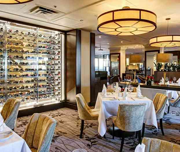 En restaurant med dekkede bord og en vegg med vinflasker. (AI-generert tekst)