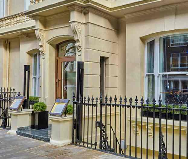 Inngang til en bygning med dekorert fasade og metallgjerde. (AI-generert tekst)