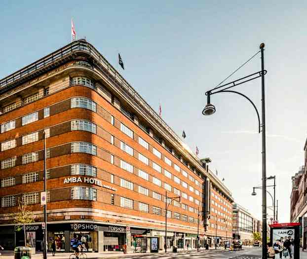 En stor teglbygning med flagg på toppen og butikker i gateplan. (AI-generert tekst)