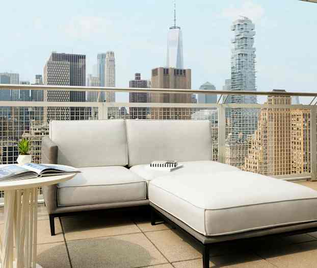 En terrasse med en lys sofa og et bord, med en bysilhuett i bakgrunnen. (AI-generert tekst)