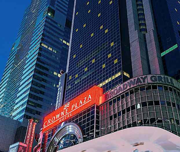 Et bilde av en høy bygning med neonskilt som viser "Crowne Plaza" og "Broadway Grill". (AI-generert tekst)