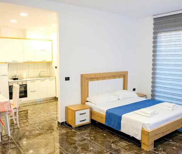 Et soverom med en dobbeltseng, bord med stoler og en liten kjøkkenkrok. (AI-generert tekst)