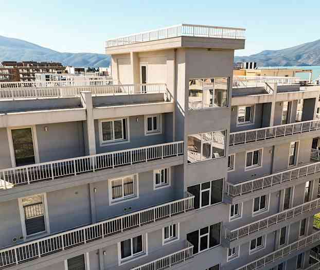 En moderne bygning med flere etasjer og balkonger, omgitt av grøntområder og omkringliggende fjell i bakgrunnen. (AI-generert tekst)